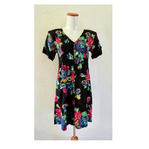 May include: A black short-sleeved dress featuring a vibrant floral pattern with red, blue, yellow, and green flowers. The dress has a V-neckline, a fitted bodice, and a skirt that falls to the knee, showcasing a bold, colorful botanical print throughout.