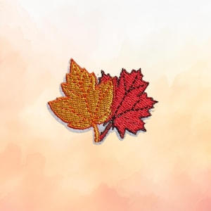 May include: An embroidered patch featuring two overlapping maple leaves. The left leaf is a vibrant golden yellow, while the right leaf is a deep, rich red. Both leaves display detailed stitched veins and serrated edges in a dense thread texture.