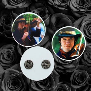 May include: Three round pinback buttons and a set of two pin backs. Two buttons feature a man playing a violin, wearing a hat and a dark coat. The pin backs are silver-colored and attached to a white circle.