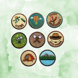 May include: A collection of embroidered patches with outdoor adventure themes. Designs include a hiker, hot air balloon, slingshot, telescope, crossed axes, a hat, a tent, and a mountain scene. Each patch has text indicating the theme.