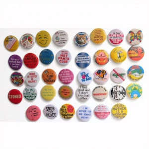 May include: A collection of forty-two circular pin-back buttons featuring various colorful designs, illustrations, and text slogans. The buttons display diverse graphics including a cat, a butterfly, a pumpkin, and phrases like Punk is Funk.