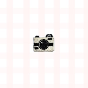 May include: Embroidered patch of a vintage camera. The camera is beige with black details, including the lens, viewfinder, and side stripes. The patch is small and square, suitable for clothing or accessories.