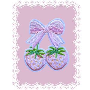 May include: Embroidered patch featuring two pink strawberries with green stems and leaves, connected by a pink bow. The patch is outlined in light blue and set against a pink background with a white lace border.