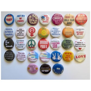 May include: A collection of 25 round button pins with various messages and designs. The buttons are colorful and feature a variety of themes, including peace, love, equality, and social justice. Some of the messages on the buttons include "Draft Beer Not Students", "I'm Back By Popular Demand", "Make Love Not Profits", "Health Care Is A Right Not A Privilege", "Woman Power", "Don't Be Racist", "All Religions Are Fairytales", "Love", and "For Women".