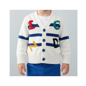 May include: A white V-neck knit cardigan featuring horizontal blue stripes and four blue buttons. The front displays colorful embroidered letters including a red I, green C, yellow Z, and black D. The garment is worn over a plain white shirt.