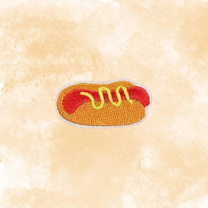 May include: Embroidered patch of a hot dog on a light orange background. The hot dog has a red sausage, yellow mustard, and a golden-brown bun. The patch is outlined in white.