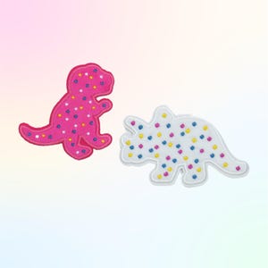 May include: Two dinosaur-shaped patches. One is pink with white, yellow, and blue dots. The other is white with the same colored dots. Both patches have a white border and are on a gradient background.