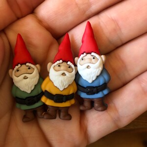 May include: Three small gnome figurines with red hats, white beards, and different colored outfits: green, yellow, and blue.