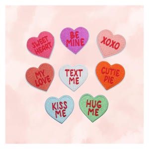 May include: A collection of heart-shaped patches in various colors, each embroidered with a different romantic message. The patches include phrases like "Sweet Heart," "Be Mine," and "XOXO," perfect for Valentine's Day or expressing affection.