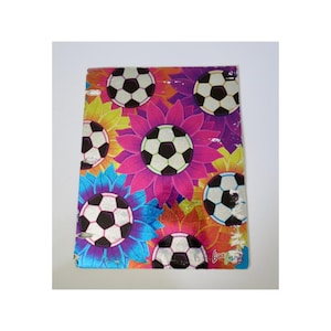 May include: A notebook with a colorful floral and soccer ball design. The cover features soccer balls in the center of flowers in shades of pink, yellow, blue, and orange. The notebook has a white background.