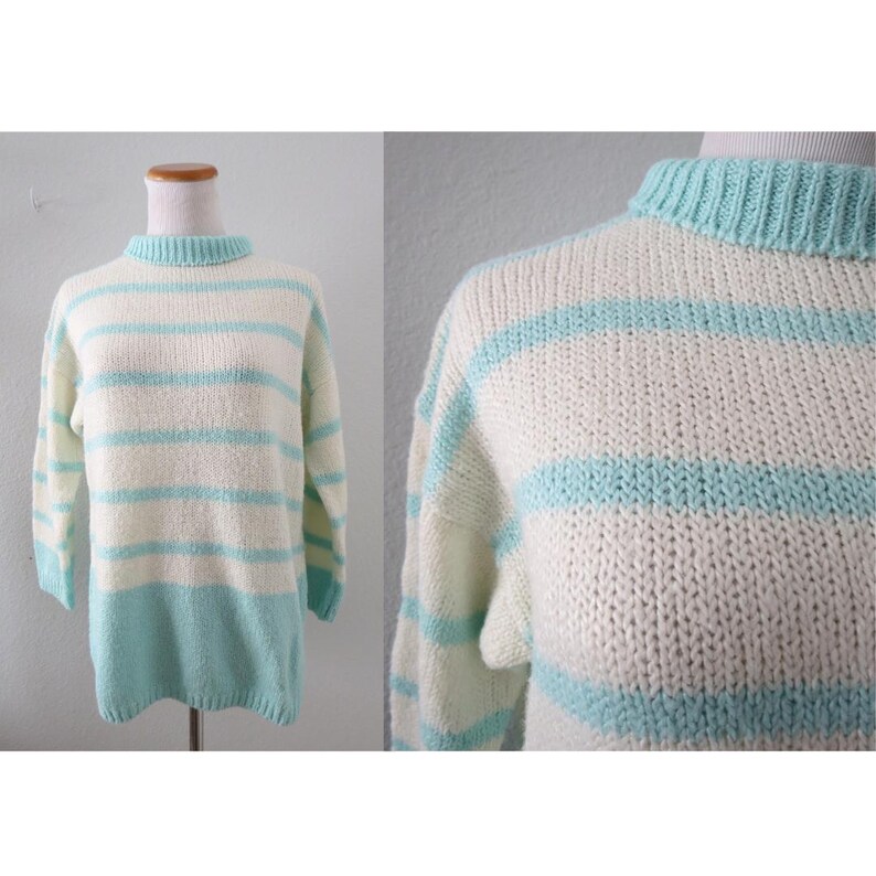 May include: A long-sleeve knit sweater featuring horizontal stripes in cream and light turquoise. The garment has a ribbed mock neck collar and a solid light turquoise hem at the bottom. The knit texture is visible throughout the entire piece.