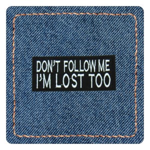 May include: A rectangular black embroidered patch with white text that reads DON'T FOLLOW ME I'M LOST TOO, centered on a blue denim fabric background with a thick orange stitched border framing the square denim piece.