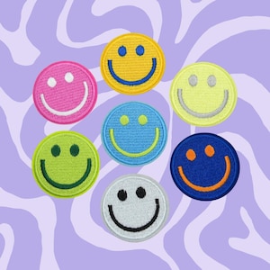 May include: Seven embroidered smiley face patches in different colors, including yellow, pink, light blue, green, blue, and white. The patches are all circular and have a simple smiley face design with two eyes and a mouth.