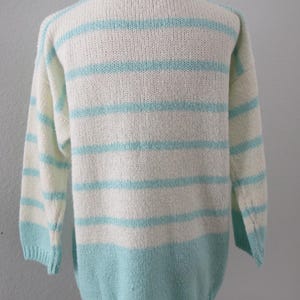 May include: A long-sleeved knit sweater featuring horizontal stripes in alternating white and light turquoise blue. The garment has a ribbed collar, ribbed cuffs, and a ribbed hemline, with a solid light turquoise blue section at the bottom.
