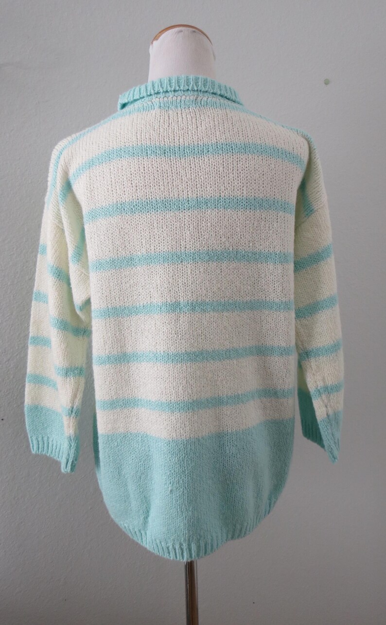 May include: A long-sleeved knit sweater featuring horizontal stripes in alternating white and light turquoise blue. The garment has a ribbed collar, ribbed cuffs, and a ribbed hemline, with a solid light turquoise blue section at the bottom.