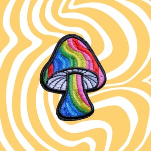May include: Embroidered mushroom patch with a rainbow design. The mushroom cap features red, orange, yellow, green, blue, and purple stripes. The stem is a vibrant rainbow color. The patch has a black border and is set against a yellow and white swirled background.