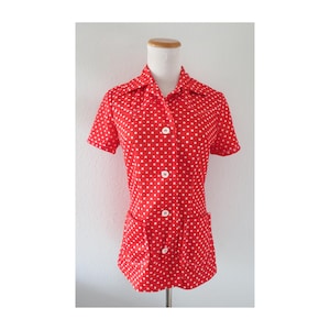 May include: Red short-sleeved shirt with white polka dots. The shirt has a collared neckline, white buttons, and two front pockets. The shirt is displayed on a mannequin.