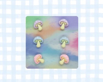 May include: Six mushroom-shaped embellishments in pastel colors: pink, blue, and lavender. Each mushroom has a light yellow stem. The mushrooms are arranged on a colorful background with a blue and white checkered pattern.