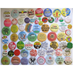 May include: A collection of vintage pinback buttons with various colorful designs and text. The buttons feature phrases like "I Love Grandpa," "Do It Your Way," and "Happiness is Being Single." Some buttons have cartoon characters.