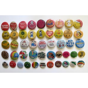 May include: A collection of colorful vintage pinback buttons with various designs and text. The buttons feature phrases like "Santa Lives!" and "I Love Me," along with cartoon characters and graphic patterns. These buttons are a fun accessory.
