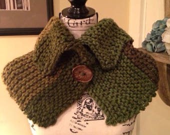 May include: A green and brown knitted cowl with a large brown button. The cowl is displayed on a white mannequin with a black base.