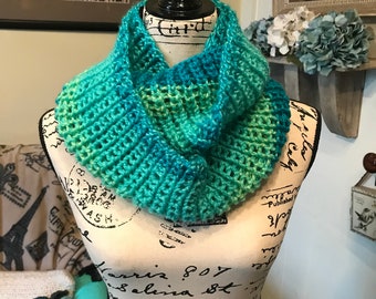 May include: A crocheted infinity scarf in shades of teal and green. The scarf is displayed on a mannequin with a vintage-style pattern.