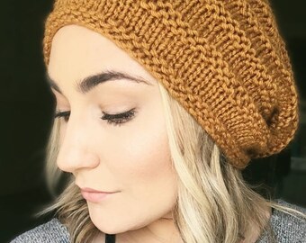 May include: A close-up of a woman wearing a mustard yellow knitted beanie. The beanie is slouchy and has a ribbed texture.