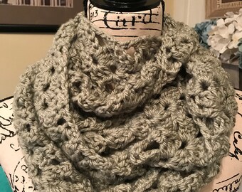 May include: A crocheted infinity scarf in a light sage green color. The scarf is made with a delicate open stitch pattern.