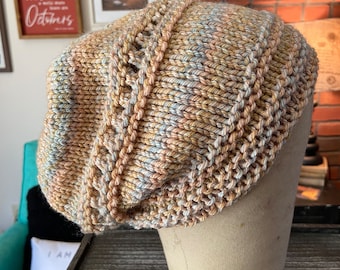 May include: A knitted hat in beige, brown, and blue colors with a textured pattern. The hat is displayed on a mannequin head.