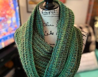 May include: A green and black crocheted infinity scarf. The scarf is made with a textured stitch and is displayed on a mannequin.