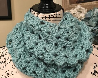 May include: A teal blue crocheted infinity scarf with a textured, open-stitch design.