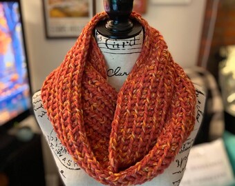 May include: A crocheted infinity scarf in a warm orange and yellow color combination. The scarf is made with a chunky yarn and has a textured stitch pattern.