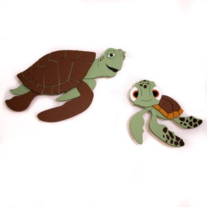Puede incluir: Dos tortugas marinas verdes con caparazones marrones. La tortuga más grande tiene una cabeza verde y un caparazón marrón con un patrón de líneas marrones. La tortuga más pequeña tiene una cabeza verde y un caparazón marrón con un patrón de manchas marrones.