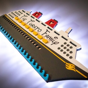 May include: A white and black wooden ship with a yellow stripe and the text "The Curato Family" on the side. The ship has a blue wave design on the bottom and a red Mickey Mouse head on the top.