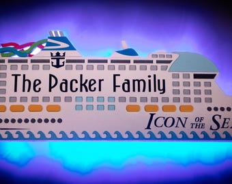 May include: A wooden cruise ship cutout, featuring the text "The Packer Family" and "Icon of the Seas". The ship is white with blue, yellow, and green details, and a blue wave pattern along the base.