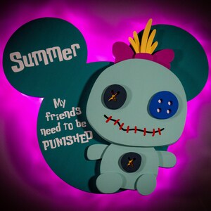 May include: A teal-colored, cartoon-style character with large button eyes and a stitched smile. The character has a bow and yellow accents on its head. The text "Summer" and "My friends need to be PUNISHED" are displayed on the teal background.