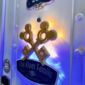 May include: A white door with gold Mickey Mouse key decor, a navy blue sign that reads "The Kiper Family" and "Disney Cruise Line", and a room number sign that reads "2630".