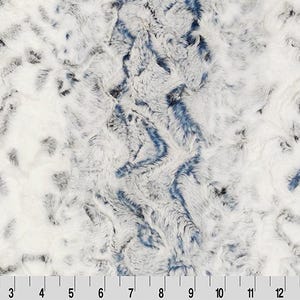 May include: Close-up of a plush fabric with a textured, mottled pattern. The fabric features a mix of white, gray, and blue hues, creating a soft, cloud-like appearance. The texture appears to be faux fur. The image includes a ruler along the bottom.