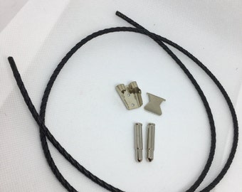 May include: A black braided leather bolo tie cord with silver-colored metal tips and clasp components. The components include a decorative clasp and two cylindrical pins. The items are arranged on a white surface.