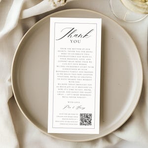 May include: A wedding reception table setting with a white card that says "Thank You" in elegant script. The card is on a white plate, with a knife and a glass of wine in the background. The card includes a QR code.