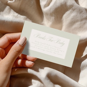 May include: A rectangular card with a sage green and white vertical striped border and a white center panel. The text reads Books For Baby, Help build Baby's library! Instead of a card, please bring a favorite children's book with a message inside.