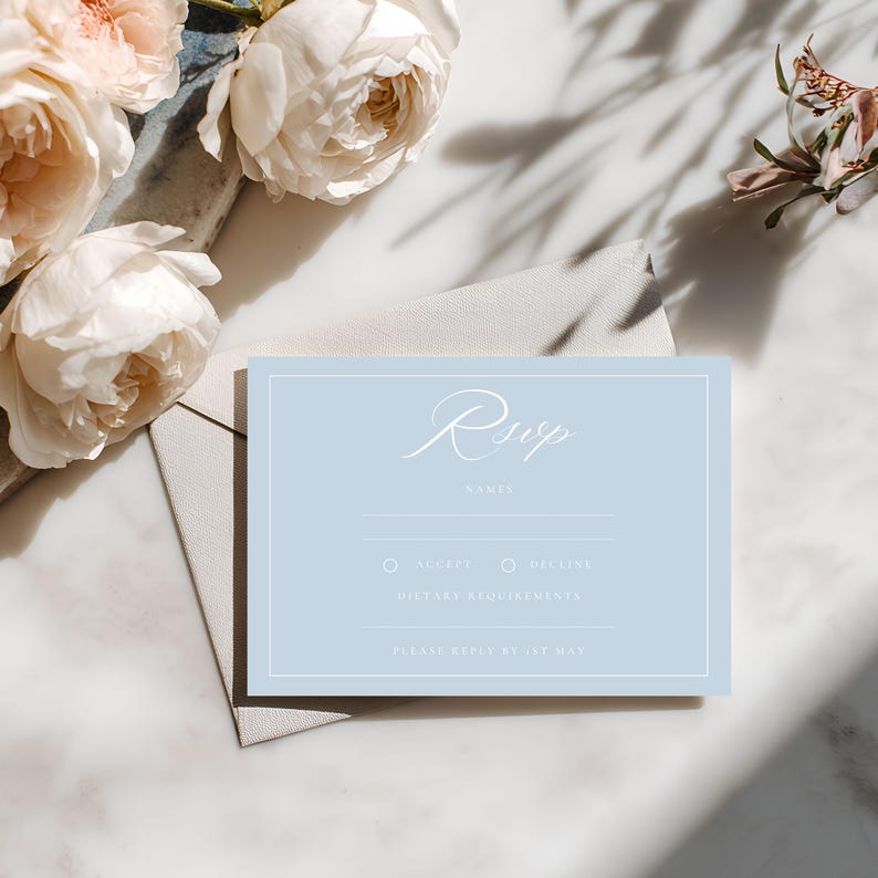 May include: A light blue RSVP card with white text and a white border. The card includes fields for names, acceptance or decline, and dietary requirements. The card is next to a light gray envelope and white and pink flowers.
