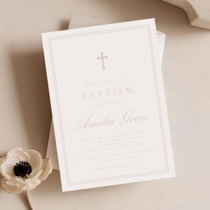 May include: A baptism invitation with a pink cross and text. The invitation is light pink with a pink border and features the name "Amelia Grace". The text includes the date, time, and location of the baptism.