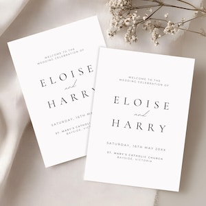 Puede incluir: Dos carteles de bienvenida de boda blancos con texto negro. Los carteles dicen "Bienvenida a la celebración de la boda de Eloise y Harry" con la fecha y el lugar. Delicadas flores blancas están en el fondo.