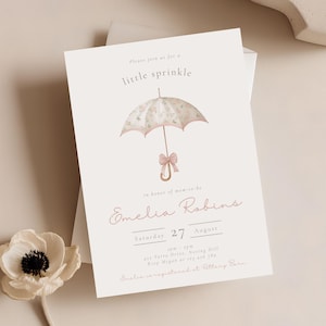 May include: A light beige invitation card with a watercolor illustration of a floral umbrella and the text "little sprinkle". The card includes event details: date, time, and location, with the name "Emelia Robins".