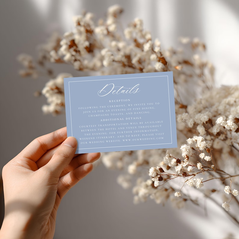 May include: A light blue wedding details card with white text and a white border. The card reads "Details" at the top, followed by information about the reception, additional details, and a website address. The card is held in front of a blurred floral background.