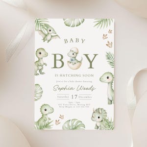 May include: A baby shower invitation card featuring watercolour illustrations of green dinosaurs, palm leaves, and footprints. The text reads: BABY BOY IS HATCHING SOON, Join us for a baby shower honouring Sophia Woods, Saturday 17 December, 2pm-5pm.