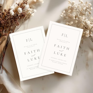Könnte beinhalten: Zwei Hochzeitseinladungskarten mit den Namen "Faith and Luke" in schwarzer Schrift. Die Karten haben ein minimalistisches Design mit einem dünnen schwarzen Rahmen und sind vor einem neutralen Hintergrund mit floralen Akzenten platziert.