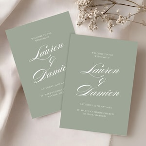 Może przedstawiać: Dwie szałwiowe zielone karty powitalne ślubne z białym kaligraficznym tekstem. Na kartach widnieje napis "Witamy na ślubie Lauren & Damien" z datą i miejscem. Delikatne białe kwiaty w tle.