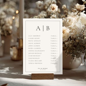 Op de afbeelding: Een cr&egrave;mekleurige trouwzitting met de initialen "A | B" bovenaan. Namen en tafelnummers staan vermeld. Het bord staat op een houten voet en is omgeven door bloemstukken. De datum "12.10.20" staat onderaan.